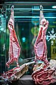 Two lamb carcasses and a beef rib hang in a Seville butcher shop, showcasing the premium quality of the meat.