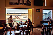 Familie beim Essen im Flughafen von Sevilla in Spanien, mit Blick auf die Landebahn und ein Flugzeug. Entspannte Atmosphäre.