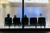 Silhouettes of people sitting in a waiting room with frosted glass, showcasing anonymity and patience while waiting.