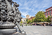 Detaillierte mythologische Figuren auf einem schmiedeeisernen Laternenpfahl auf der Plaza de Bib Rambla mit der Kathedrale im Hintergrund in Granada, Spanien.