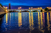 Die bei Einbruch der Dunkelheit beleuchtete Triana-Brücke mit Spiegelungen auf dem Fluss Guadalquivir in Sevilla, Andalusien, Spanien.