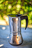 Stainless steel coffee maker on a sunny outdoor table in Fuenteheridos, Huelva. Capturing a nostalgic morning coffee vibe.