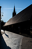 Sunset view of the historic Les Halles marketplace in Questembert, Brittany, France. Featuring cobblestone streets, shadows, and the silhouette of a church steeple.