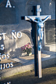 Nahaufnahme eines Kruzifixes und eines Grabsteins auf einem katholischen Friedhof in Aznalcazar, Provinz Sevilla, Andalusien, Spanien, der eine feierliche und respektvolle Atmosphäre widerspiegelt.