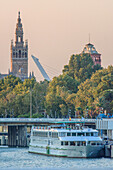 A cruise ship docked on the Guadalquivir River with Alamillo Bridge and Giralda in the background, Seville, Spain.