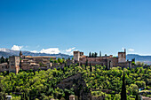 Blick auf die Alhambra von Albaycin, Granada, Spanien, mit ihrer historischen Architektur, umgeben von üppigem Grün und fernen Bergen.