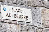 Nahaufnahme eines Straßenschilds am Place Au Beurre in Quimper, Bretagne, Frankreich. Steinmauer im Hintergrund und Wappen sichtbar.