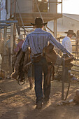 A saddle bronc cowboy carries his special bucking saddle to the bucking chutes at a rodeo in rural Utah.