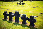 A peaceful scene at the German military cemetery in Normandy, France, showcasing rows of stone crosses on lush green grass.