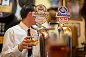 A bartender pours beer at a traditional bar in Granada, Andalusia, Spain. The scene captures the local culture and the enjoyment of fine beverages.