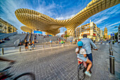 Vibrant street scene with people walking and cycling near the Metropol Parasol, a major landmark in Seville, Spain.