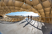 Two people walking on the iconic Las Setas structure in Seville, Andalusia, Spain, under a clear blue sky.