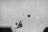 A young boy playing soccer on a cobblestone street in Seville, Spain on a sunny day.