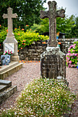 Close up of ancient gravestones covered with moss and flowers in Guehenno, Brittany, France. Serene and tranquil cemetery scene.