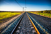 Eisenbahnschienen, die sich durch die malerische Landschaft von Carrion de los Cespedes in der Provinz Sevilla, Andalusien, Spanien, ziehen. Gelassene Landschaft mit leuchtenden Feldern.