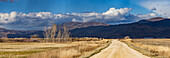 Empty dirt road leading to foothills under stormy skies