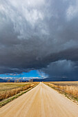 Gewitterwolken über einer leeren unbefestigten Straße in einer ländlichen Landschaft