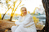 Portrait of woman in white sweater sitting by river in autumn