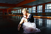 Pensive ballerina sitting on floor in ballet studio