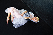 Portrait of ballerina wrapped in white tulle lying on floor in ballet studio