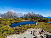 Frau springt in Landschaft im Fiordland-Nationalpark