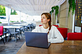 Pensive woman with laptop at cafe table