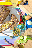 Vollkornbrot mit Blütenbutter, Gurkenscheiben und Eiern auf bunter Tischdecke