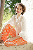 Brunette woman in cream-coloured blouse and orange-patterned trousers