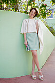 Young woman in pastel green skirt and white blouse with jacket in front of a green wall