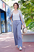 Young woman in casual business outfit walking outside with straw hat