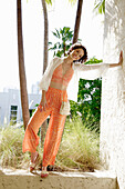 Woman in striped orange and white summer clothing in front of palm trees