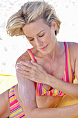 Woman wearing colourful striped swimwear and applying sunscreen