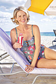 Woman in floral swimming costume, relaxing on a beach lounger under parasol