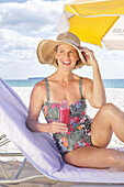 Woman in summer clothes with a drink on the beach under a yellow parasol