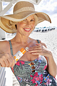 Woman in floral swimming costume applies sunscreen, straw hat