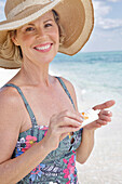 Woman on the beach in floral swimming costume and straw hat, with sun cream