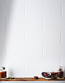 Indian spices arranged on a wooden shelf in front of a white tiled wall