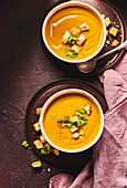 Two bowls of pumpkin and sweet potato soup with croutons