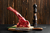 Raw ribeye steak on wooden board with pepper mill