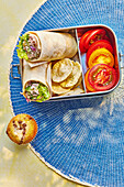 Snack box filled with spicy tuna wrap, tomato slices and crisps