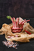 Raw rack of lamb on paper with rosemary, chilli and garlic