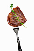Grilled beef steak on a fork with herb sprig