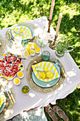 Sommerlicher Gartentisch mit Melonen-Feta-Salat, Zitronen und gelb-weiß gestreiften Tellern in Zitronenform