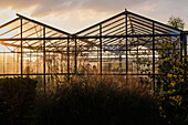 Gewächshaus im Sonnenuntergang mit blühendem Garten im Vordergrund