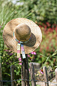 Strohhut mit buntem Band auf Holzzaun im Garten
