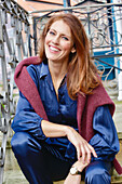 Red-haired woman in blue satin blouse and burgundy knitted jumper over her shoulders