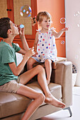 Brother and sister blowing bubbles at home