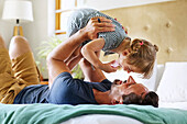 Father playing with daughter on bed