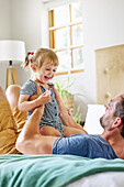 Father playing with daughter on bed