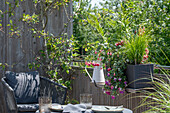 Wasserspeicherkasten mit Fuchsien (Fuchsia), Farn und Gräser an Balkongeländer hängend neben Sitzplatz und gedeckter Tisch